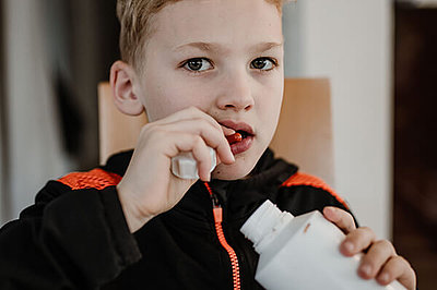 Ein Junge - ca. 8 Jahre alt - hat eine Medikamentendose in der Hand und nimmt gerade Medikamente ein.