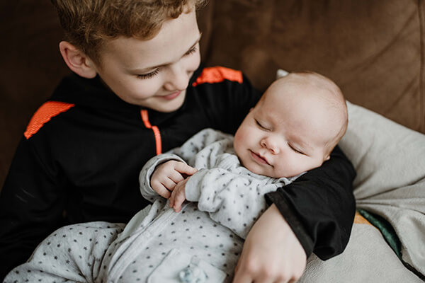 Ein etwa 8-jähriger Junge hat ein schlafendes Baby auf dem Arm.