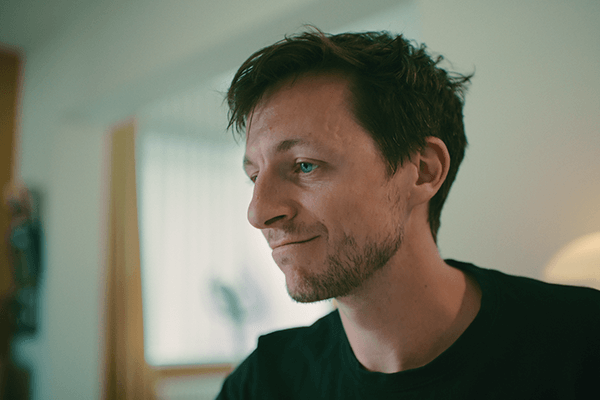 Porträt von Mark: Mann, Mitte Dreißig, von der Seite, dunkle Haare, dunkles Shirt. 