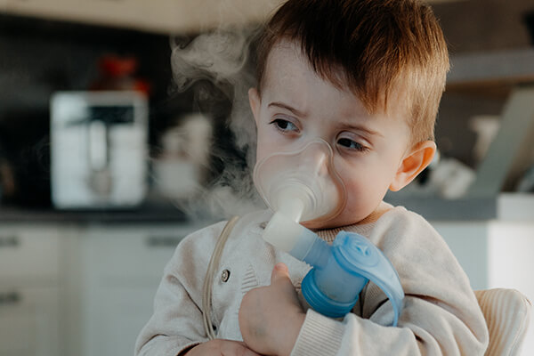 Theo inhaliert. Etwa zweijähriger Junge hält ein Inhaliergerät in den Armen und inhaliert wahrscheinlich eine Kochsalzlösung.